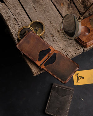 El dikişi taba Crazy Deri bifold cüzdan, açık pozisyonda metal para klipsi ve dört kart gözüyle — koyu kahve tonlarında Full Grain (Üst Tabaka) derinin doğal leke ve renk geçişleri, krem renkli kontrast el dikişi ve yanında koyu taupe renk ikinci renk seçeneğiyle birlikte Kooka Leathercraft imzasıyla sunuluyor.