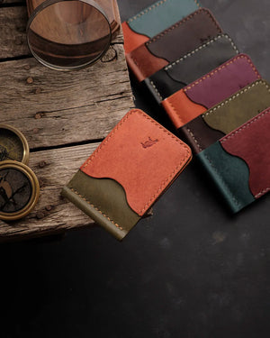 El dikişi deri cüzdan koleksiyonu; ön planda turuncu ve olive renk kombinasyonlu PUEBLO deri model, scallop kesimli kart gözü açıklığı, kontrastlı sarı el dikişi ve emboss kuş logosuyla öne çıkıyor. Arka planda teal, bordo, mor, gri ve kahverengi renk seçenekleriyle sergilenen tam koleksiyon, zengin doku ve mat yüzey kalitesiyle dikkat çekiyor.