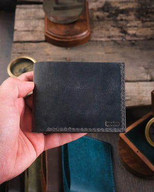 El yapımı gri crazy deri Torn kompakt cüzdan kapalı halde elde tutuluş, Kooka Leather saraç dikişi detaylı bifold tasarım