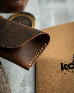 El dikişi deri kalemlik açık ağız detayı — KOOKA Leathercraft imzalı Crazy Deri taba rengi yatay kalemliğin kıvrımlı üst kapağı ve köşe dikişleri yakın çekimde; Full Grain (Üst Tabaka) deri yüzeyindeki çizik izi ve pull-up etkisi dokusu net şekilde görünürken el dikişi beyaz iplik dikişleri keskin bir işçilik kalitesine işaret ediyor.