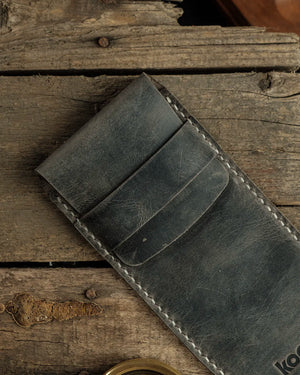 El dikişi deri kalemlik Crazy Deri gri renk mıknatıssız kapak tokası ve krem kontrastlı el dikişiyle öne çıkan kooka Dikey Kalemlik, charcoal tonlarında distressed yüzey dokusu ve çizik izi efektiyle sert mat görünüm sunar; kapaklı ön kısmın yapısı ve deri askı bendi açıkça seçilebilmektedir.