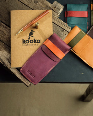 El dikişi Pueblo deri kalemlik, mor gövde ve camel kontrast kapama kayışıyla öne çıkan Kooka Leathercraft işçiliği; sarı iplik dikişler ve kabartma logo detayıyla tamamlanmış Full Grain (Üst Tabaka) deri yüzey