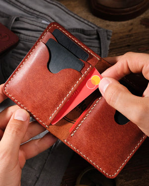 Eller Kooka OZN taba cognac tam dane deri bifold cüzdanı açık tutuyor; kırmızı Mastercard kredi kartı scallop kesimli kart yuvasına yerleştiriliyor, iç bölmede siyah kartlar görünüyor, krem renkli el dikişi ve pull-up deri dokusu ön planda