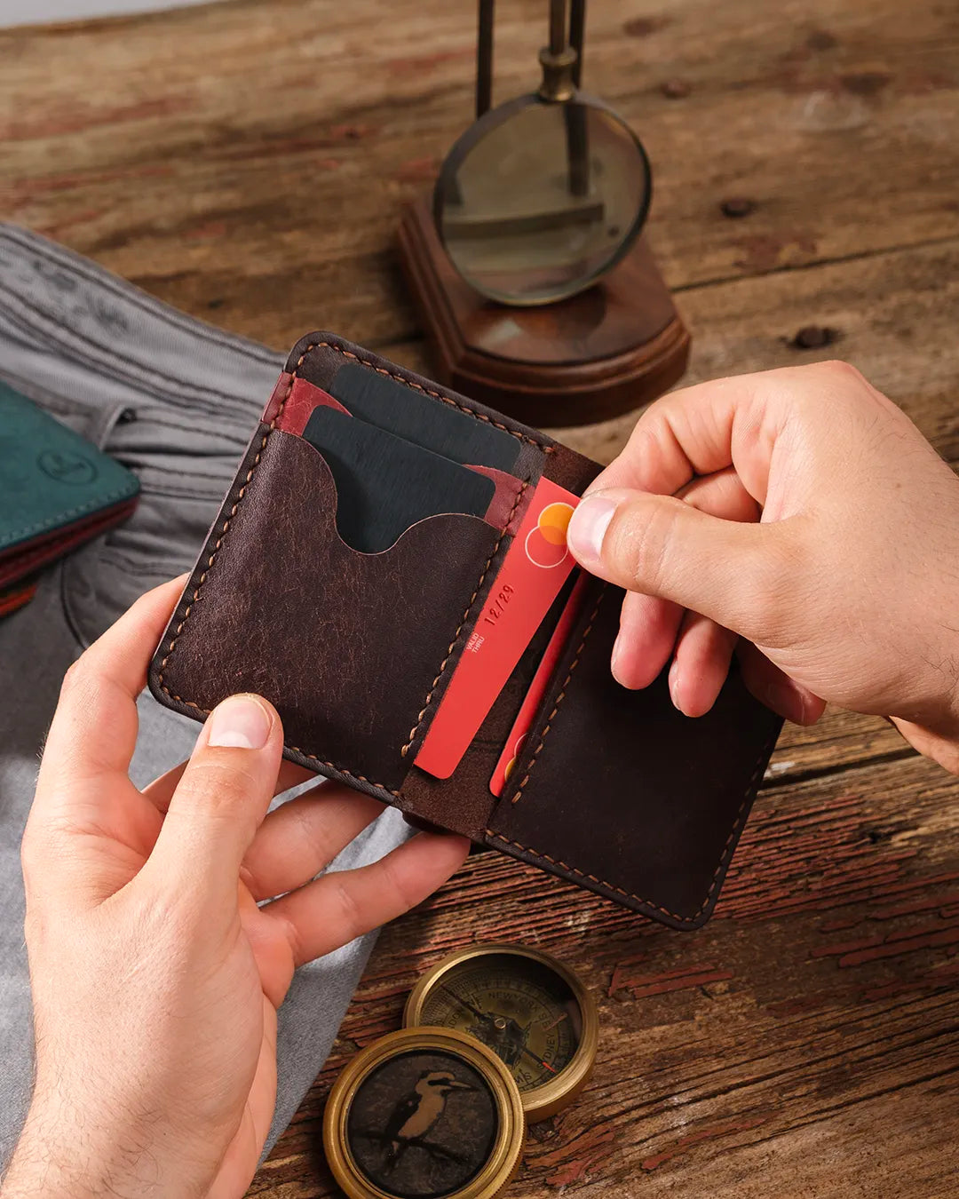 Elde tutulan açık bordo-kahverengi pueblo bifold cüzdan, kart slotundan pratik kart çıkarma hareketi görünümü, Kooka Leather