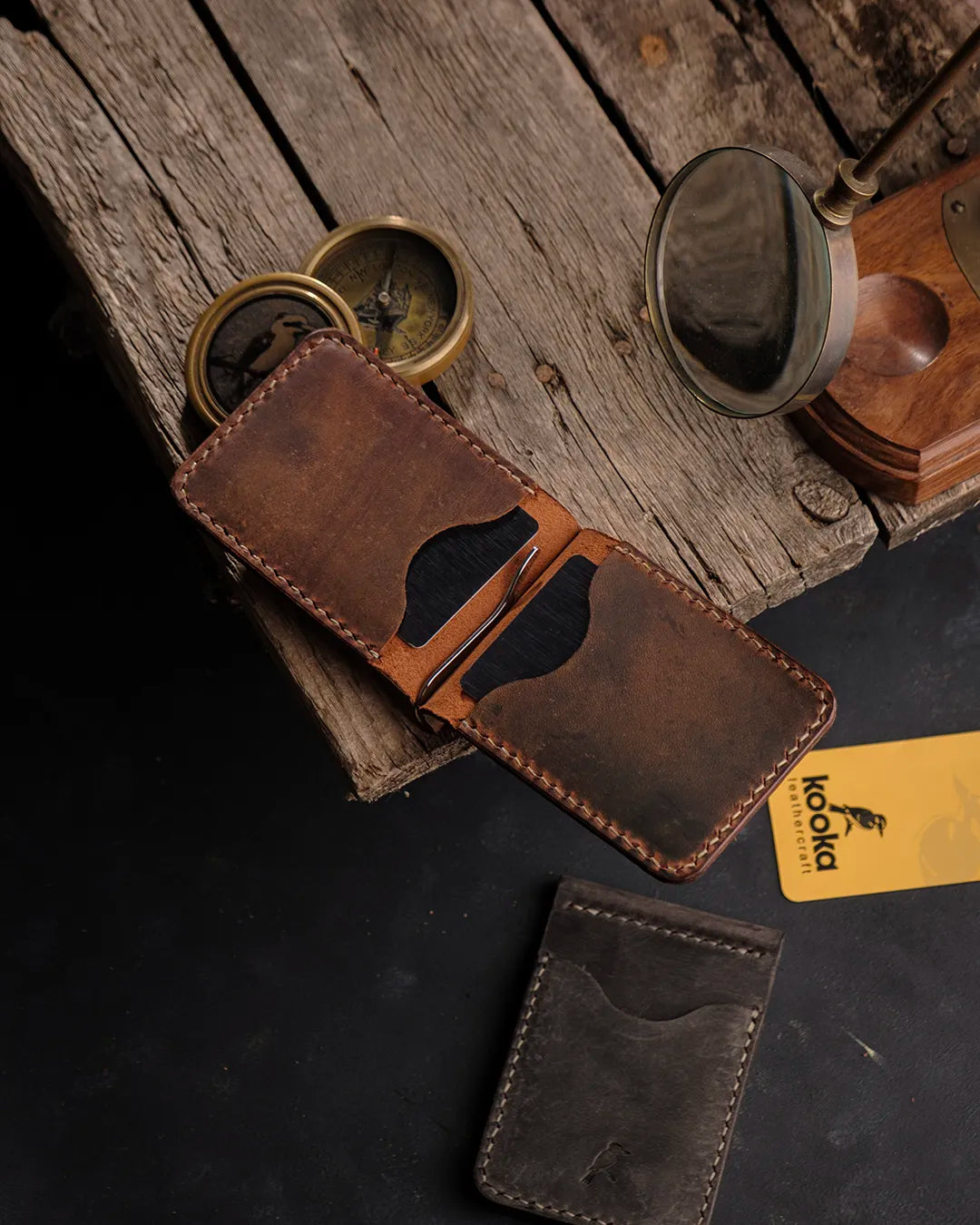 El dikişi taba Crazy Deri bifold cüzdan, açık pozisyonda metal para klipsi ve dört kart gözüyle — koyu kahve tonlarında Full Grain (Üst Tabaka) derinin doğal leke ve renk geçişleri, krem renkli kontrast el dikişi ve yanında koyu taupe renk ikinci renk seçeneğiyle birlikte Kooka Leathercraft imzasıyla sunuluyor.