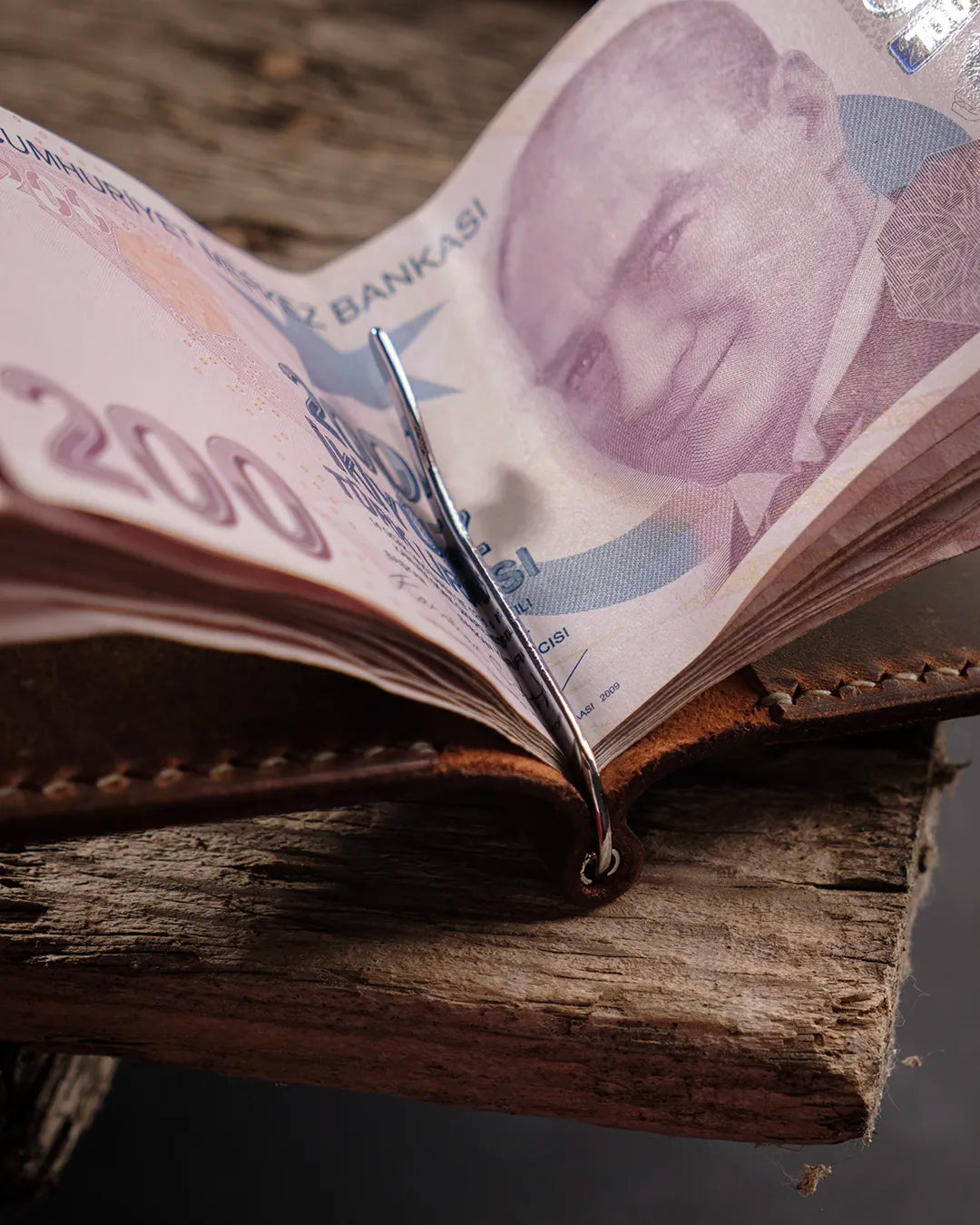 El dikişi deri cüzdan metal para klipsi detayı: taba rengi Crazy Deri yüzeyin doğal dokusu ve dikiş izleriyle birlikte polisaj çelik yay klipsin banknot tutuş açısından yakın çekim görünümü, Full Grain (Üst Tabaka) derinin zengin kahverengi tonu ve işlenmiş kenar kalitesiyle öne çıkan CRAZY model bifold cüzdan.