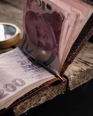El dikişi kahverengi PUEBLO deri para klipsli cüzdan, metal para klipsiyle katlanmış banknotları sıkıca tutan taba iç yüzeyiyle birlikte yakın plan görünümü; sıkı el dikişi ve burnished kenar işçiliğiyle öne çıkan artisanal tasarım.