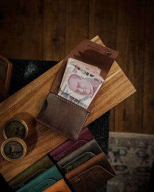 El dikişi deri cüzdan, koyu kahverengi PUEBLO deri yüzeyli kooka STYLE modeli açık konumda; nakit bölmesinde Türk lirası banknotları görünür halde, krem renkli kontrastlı el dikişi dikişleriyle detaylandırılmış iç yapı ve antik pirinç çıtçıt kapama ile birlikte farklı renk seçenekleriyle birlikte sergileniyor.