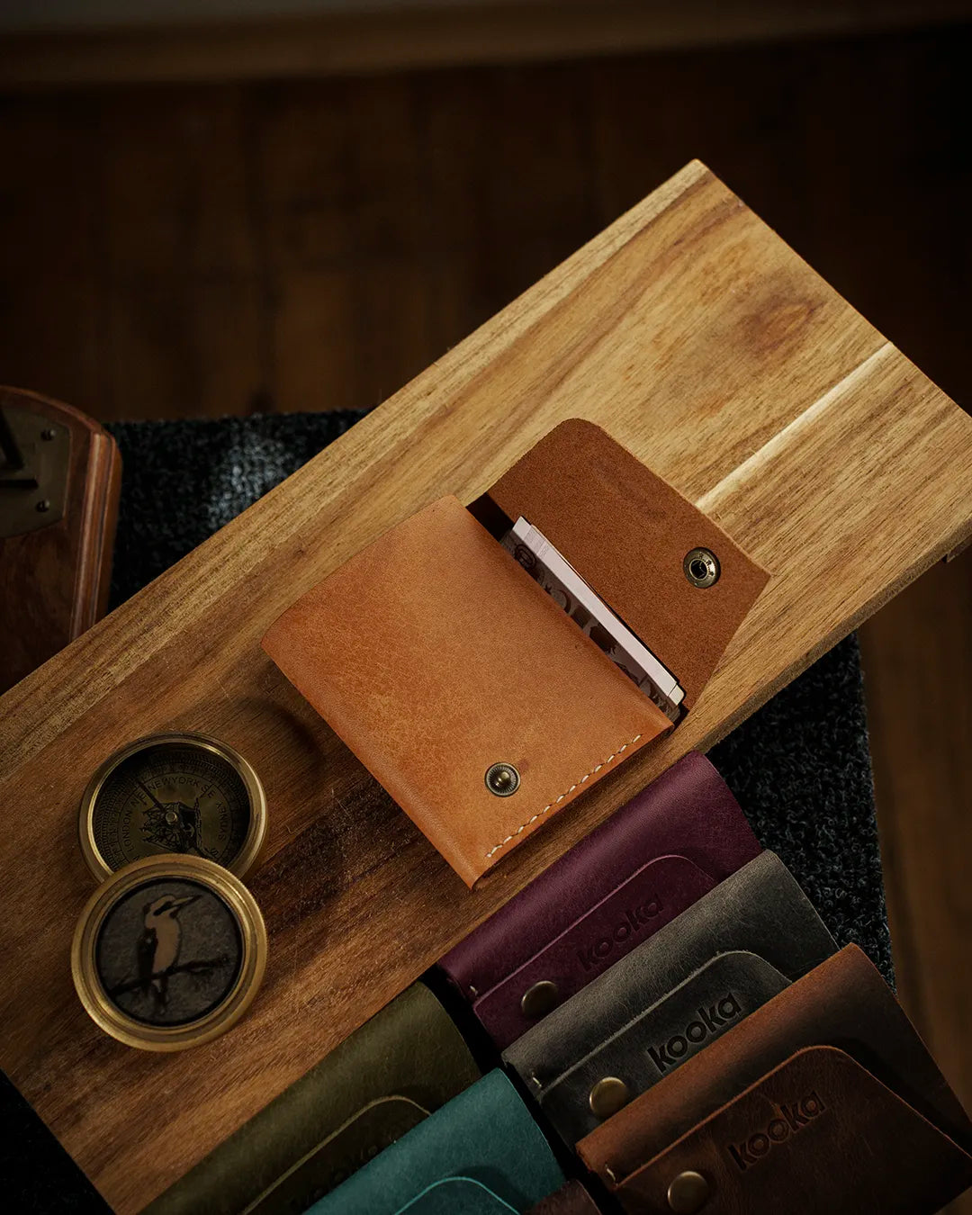 Hakiki Pueblo deri bifold cüzdan camel rengi, açık konumda kart gözleri görünür halde, antik pirinç çıtçıt kapama detaylı; ön planda kooka STYLE serisi tüm renk seçenekleri (bordo, koyu gri, kahverengi, zümrüt yeşili) yan yana sıralanmış, her birinde kabartma kooka logosu ve el dikişi dikiş detayı seçilebilir.