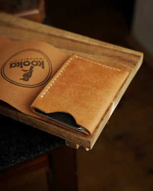 El dikişi deri cüzdan, camel renkli PUEBLO derisi ile üretilmiş kooka STYLE modeli; krem rengi saddle stitch dikiş detayı, pull-up deri yüzeyinin doğal ton geçişleri ve kart bölmesinden hafifçe çıkan kartlarla kapalı pozisyonda yan açıdan görünüm.