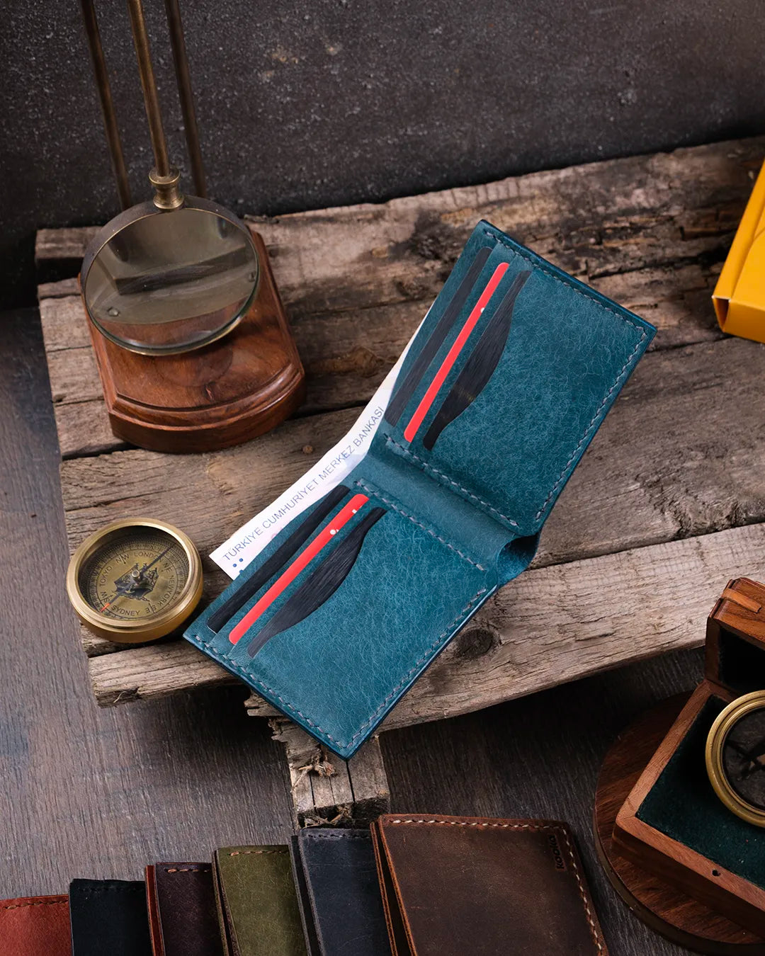 Ahşap masa üzerinde mavi bifold pueblo deri cüzdan tamamen dolu halde, kart ve para kapasitesi kullanım senaryosunda görünüyor, Kooka Leather