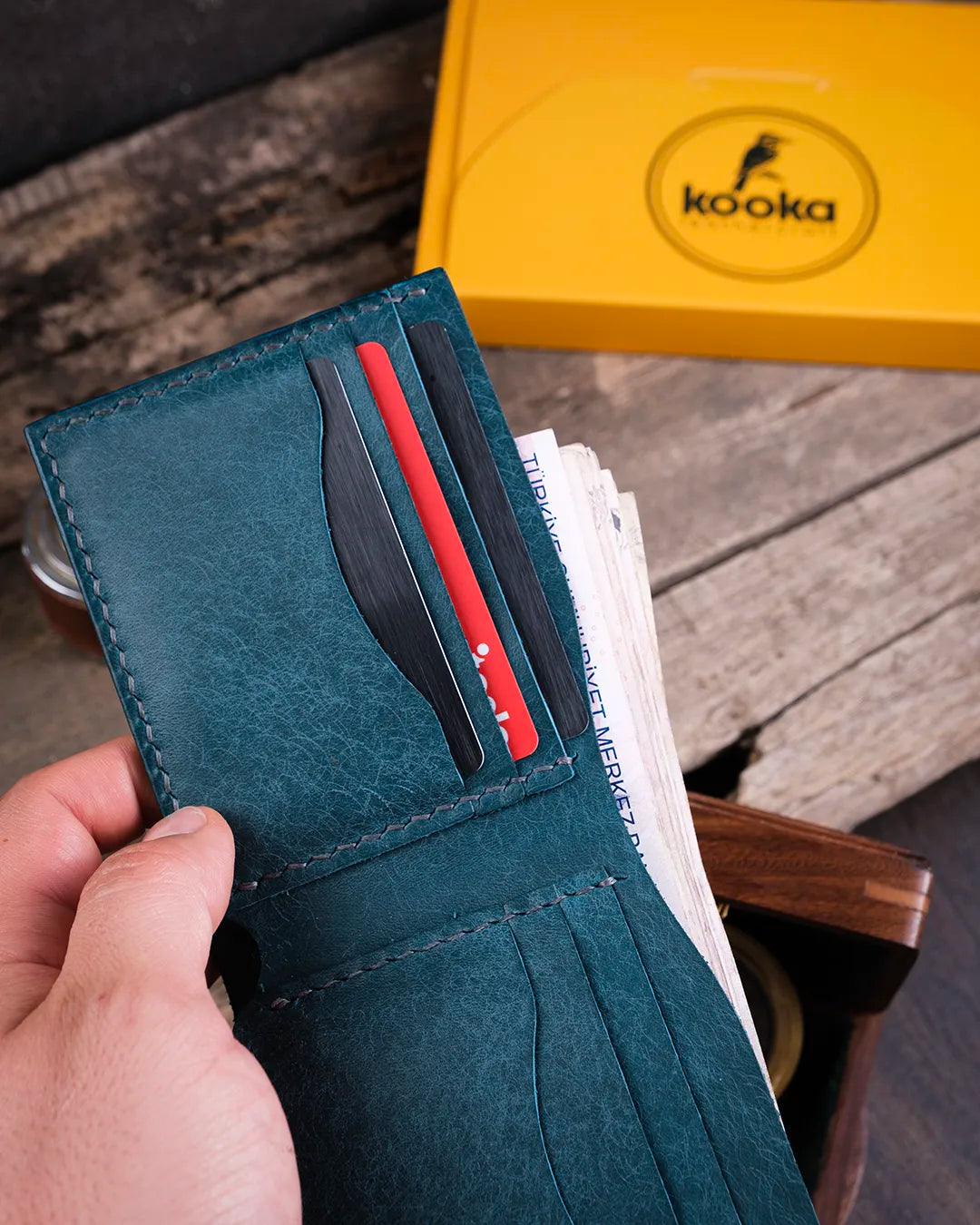 Rustik ahşap yüzeyde mavi el yapımı pueblo deri cüzdan, kartlık bölümlerinin yakın çekiminde el dikişi kalitesi öne çıkıyor, Kooka Leather