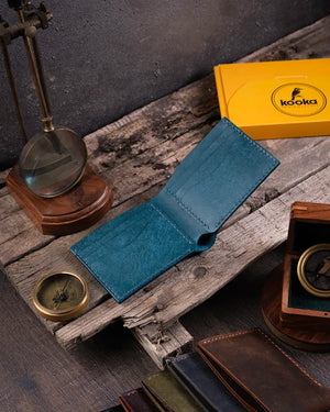Ahşap masa üzerinde mavi pueblo deri bifold cüzdan açık halde 6 kartlık bölmeli iç tasarımı sergiliyor, Kooka Leather el dikişi