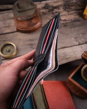 Ahşap zeminde kağıt para bölmesi hacmini gösteren siyah pueblo deri bifold cüzdan yakın çekim, Kooka Leather el dikişi