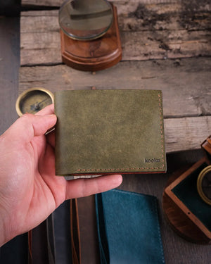 El yapımı pueblo deri bifold cüzdanın kapalı haldeki rustik görünümü, ahşap yüzeyde elde tutuş, Kooka Leather zanaat işçiliği