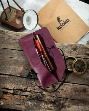 El dikişi mor Pueblo deri kalemlik, açık pozisyonda içinde kalemler ve yazı araçlarıyla — KOOKA Leathercraft imzalı Full Grain (Üst Tabaka) deri yüzeyin kadifemsi dokusu, siyah bağcık sarma kapama sistemi ve sağlam el işçiliğiyle öne çıkan 21.5x6.5 cm yatay kalemlik.