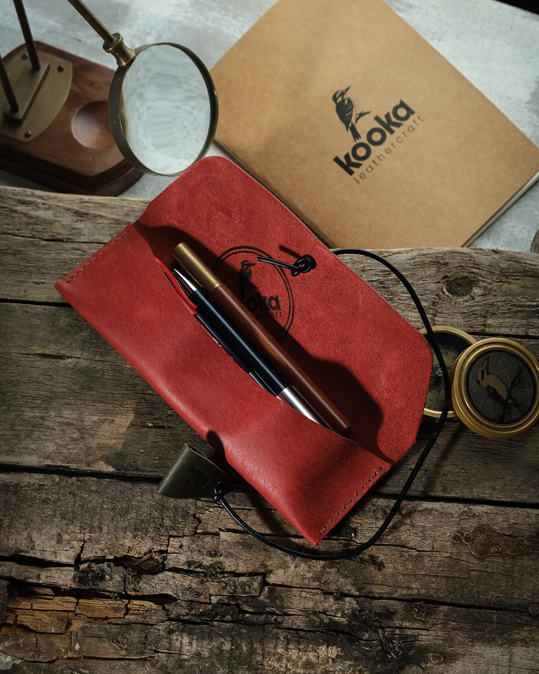 Hakiki deri el işçiliği kalemlik, canlı kırmızı tonlu PUEBLO derisiyle üretilmiş Kooka Leathercraft Yatay Kalemlik, açık konumda içinde kalemlerle görünüyor; suet iç yüzeyi, dairesel kookaburra marka baskısı ve kenar boyunca düzenli el dikişiyle artisanal kaliteyi yansıtıyor.