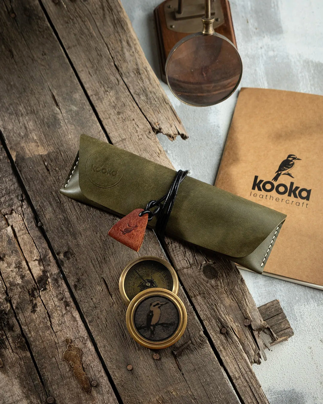 El dikişi PUEBLO deri kalemlik, zeytin yeşili rengi ve mat kadifemsi yüzey dokusuyla öne çıkan Kooka Leathercraft imzalı tam kapamalı tasarım; sargılı deri kordon kilidi ve bronz rengi üçgen çekme askısıyla tamamlanan, Full Grain (Üst Tabaka) derinin doğal karakterini yansıtan el yapımı kalem çantası.